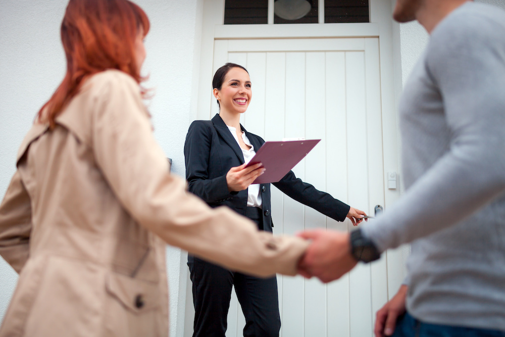 Real estate agent near door inviting young couple to enter house for visit